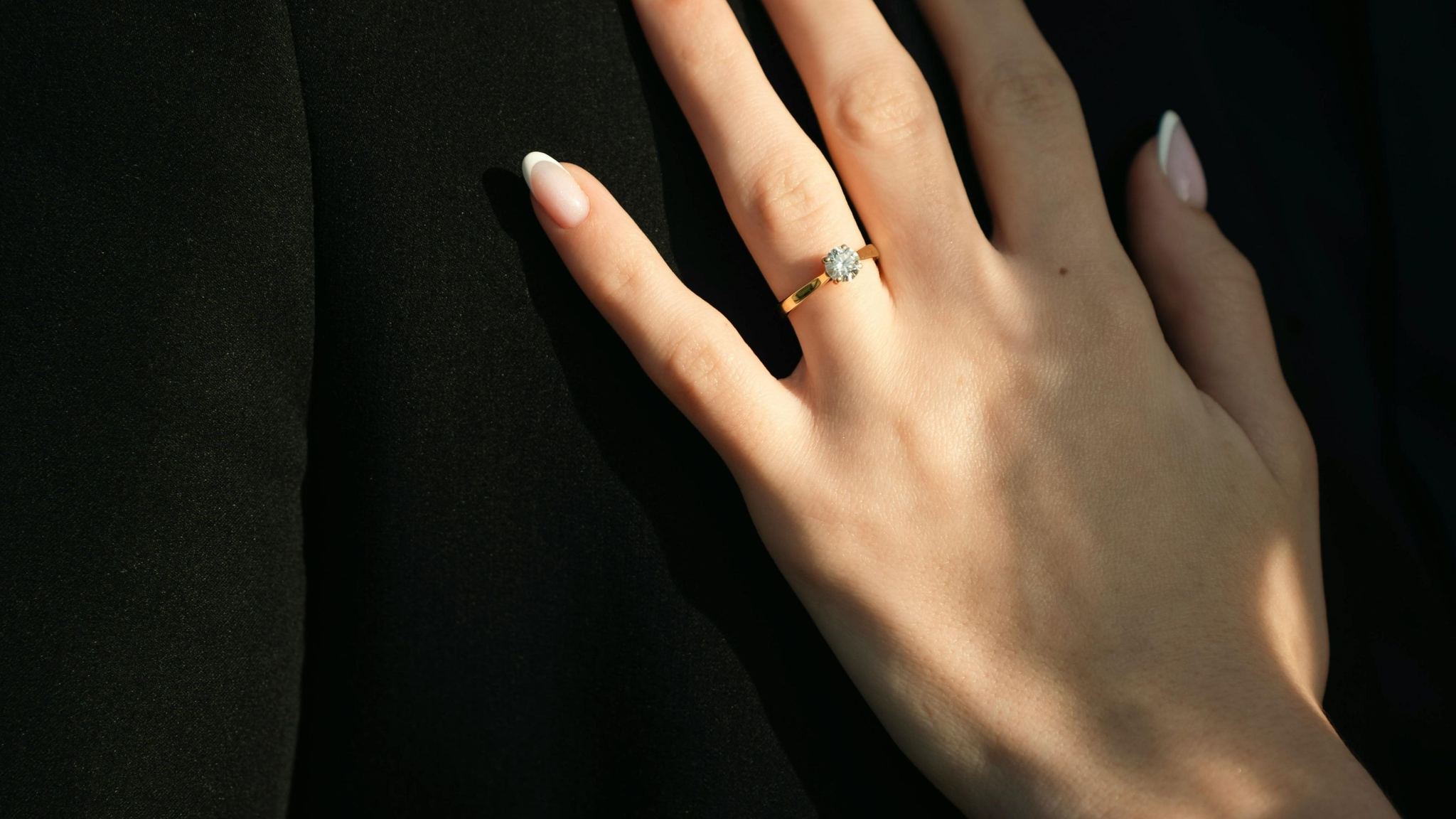Mano con anillo de compromiso solitario en oro, sobre fondo oscuro